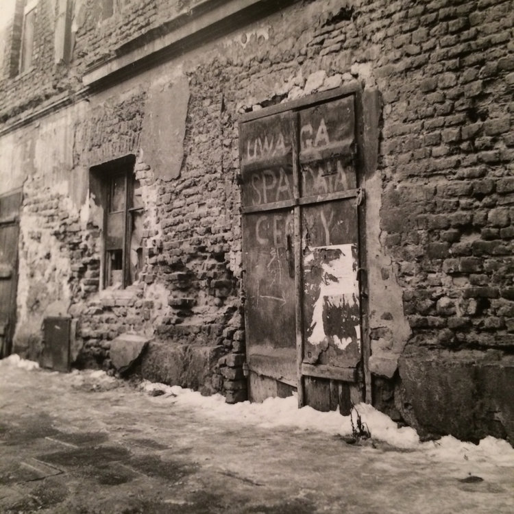 Brick wall in an old Jewish Quarter in Krakow, PL. Deteriorating due to luck of funds for renovations. Sign on the door saying "Alert Falling Bricks". Situation from 1991.