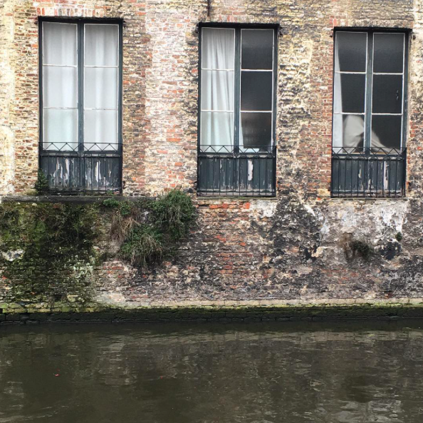 Bruges, Belgium. Brick wall of a building surrounded by water of the canal.