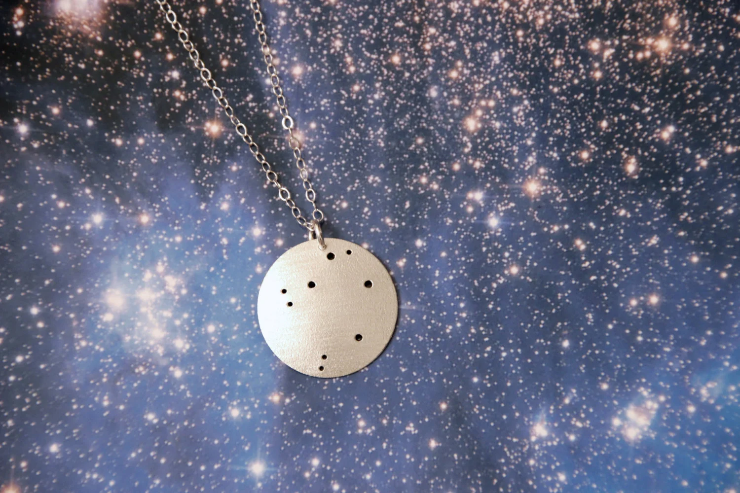 Round brushed silver pendant has 9 small holes drilled to match the Libra constellation. Pendant is slightly domed and attached to an open-link silver chain with a silver jump ring.