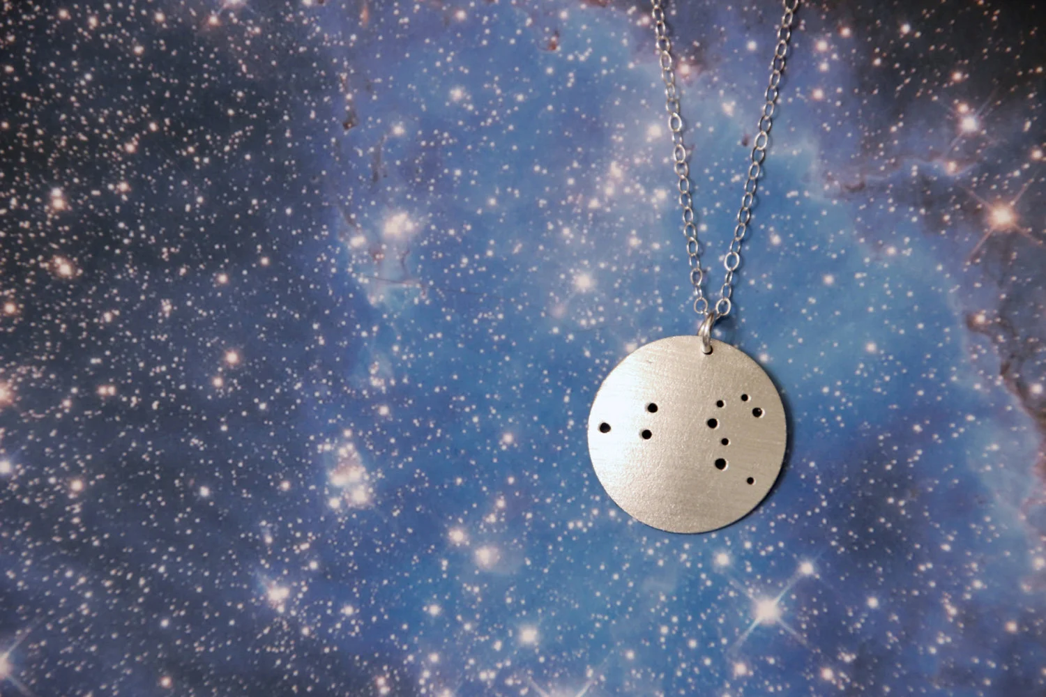 Round brushed silver pendant has 10 small holes drilled to match the Leo constellation. Pendant is slightly domed and attached to an open-link silver chain with a silver jump ring.