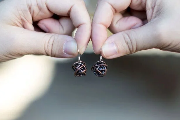 Antiqued copper wrapped wire ball earrings on sterling silver earwires in hands
