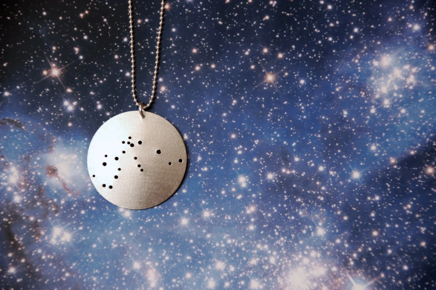 Round brushed silver pendant has 20 small holes drilled to match the Aquarius constellation. Pendant is slightly domed and attached to a narrow silver ball chain with a silver jump ring.