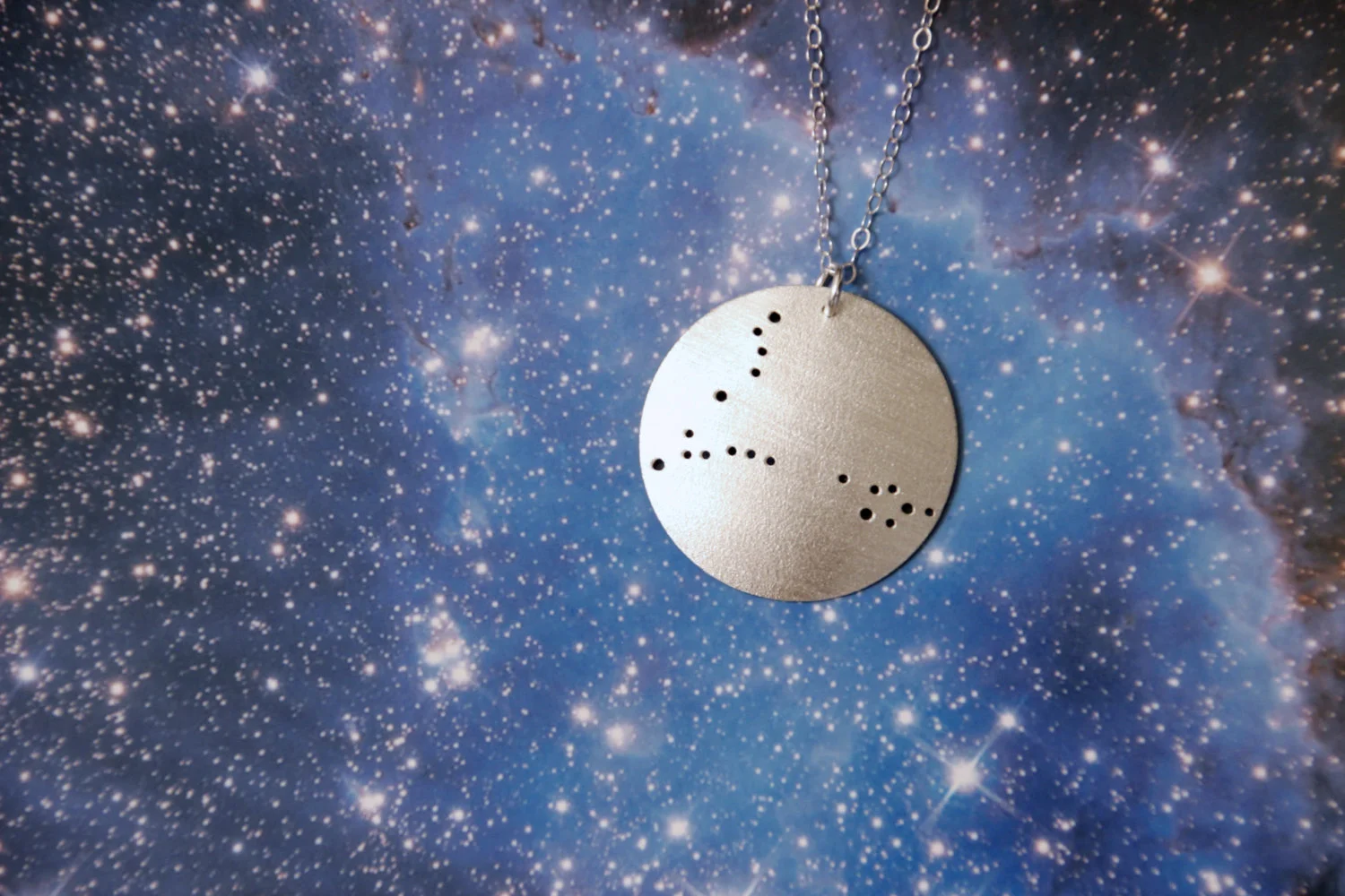 Round brushed silver pendant has 19 small holes drilled to match the Pisces constellation. Pendant is slightly domed and attached to an open-link silver chain with a silver jump ring.