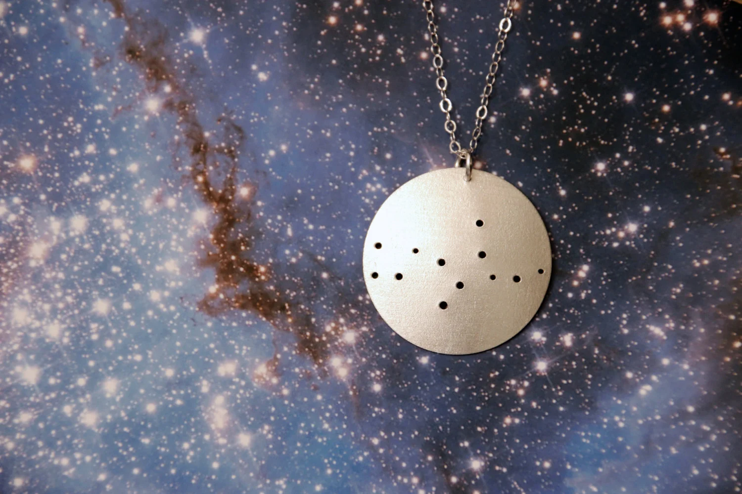 Round brushed silver pendant has 12 small holes drilled to match the Virgo constellation. Pendant is slightly domed and attached to an open-link silver chain with a silver jump ring.