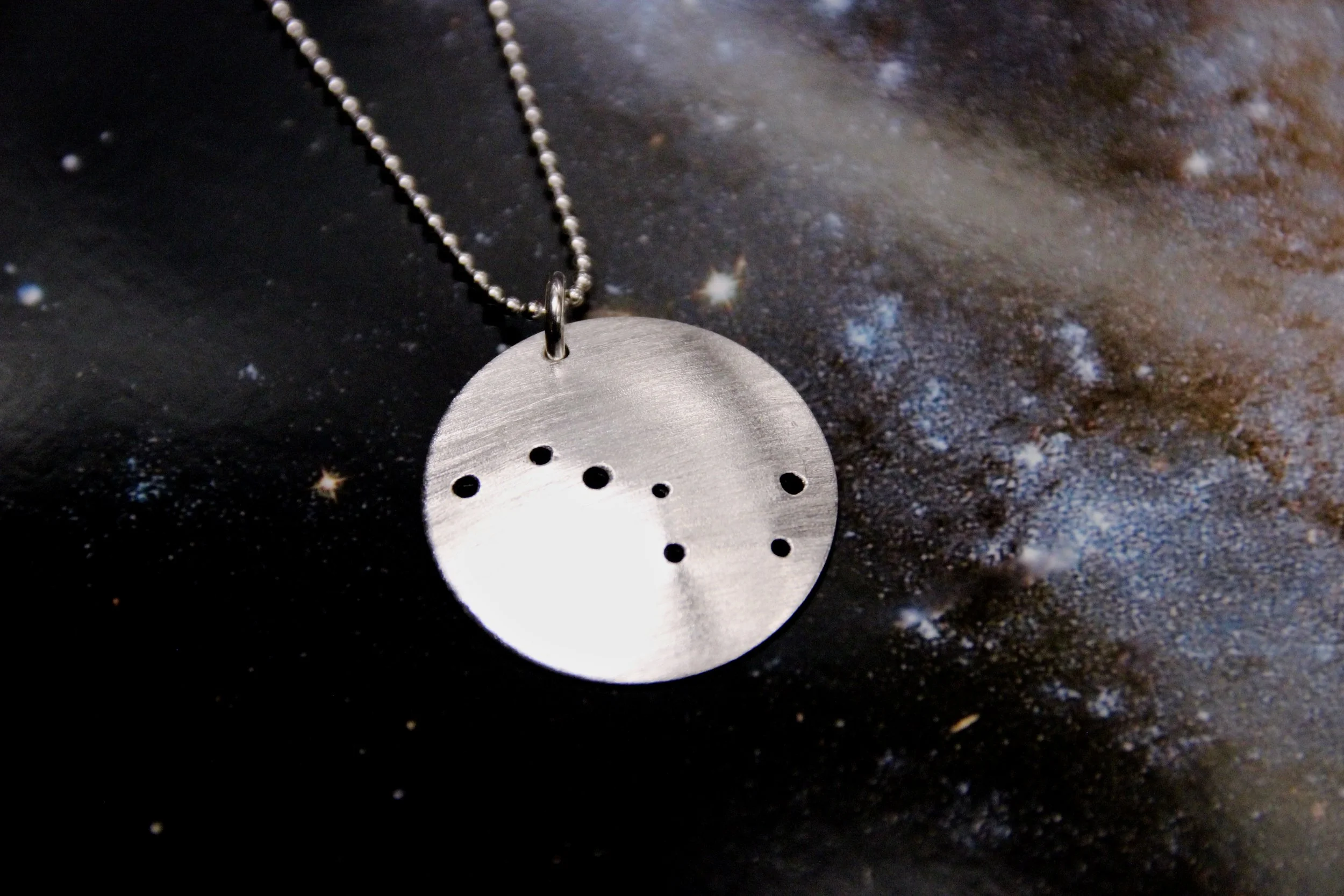 Round brushed silver pendant has 7 small holes drilled to match the Big Dipper constellation. Pendant is slightly domed and attached to a narrow silver ball chain with a silver jump ring.