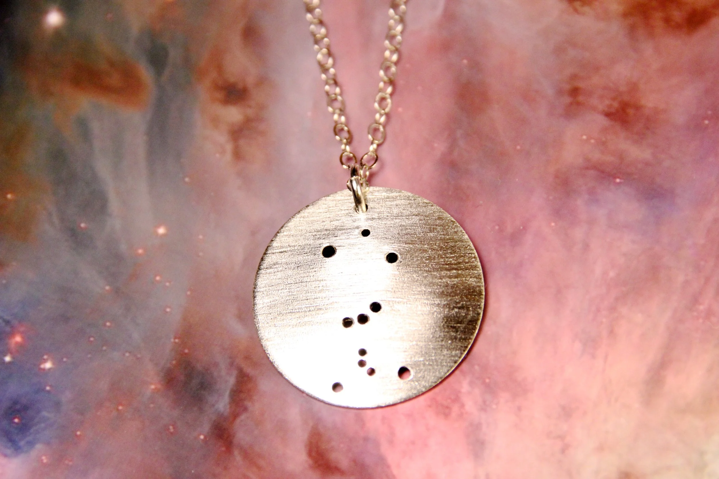 Round brushed silver pendant has 11 small holes drilled to match the most recognizable part of the Orion constellation. Pendant is slightly domed and attached to an open-link silver chain.