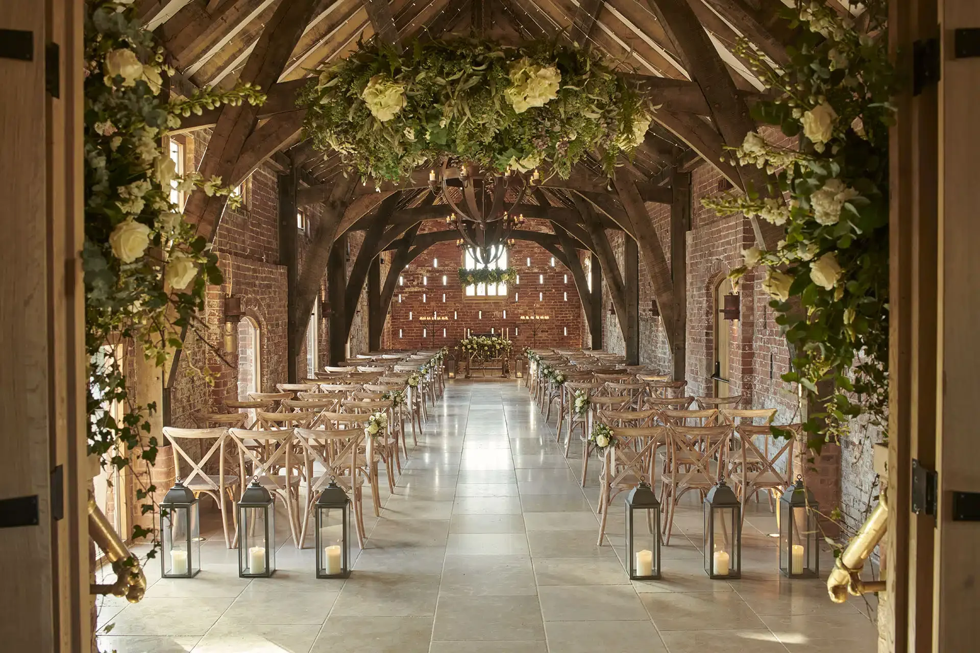 Interior of Grangefields wedding venue with wooden beams, floral decorations, and lanterns lining an aisle, prepared for a ceremony.