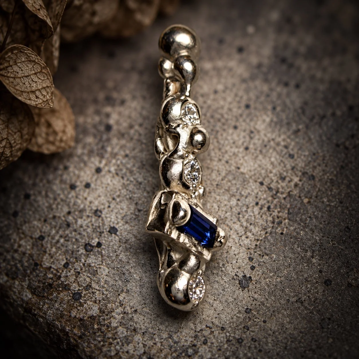 Close-up of hand-carved Fragments silver earring with lab-grown diamond, moissanite and baguette sapphire settings