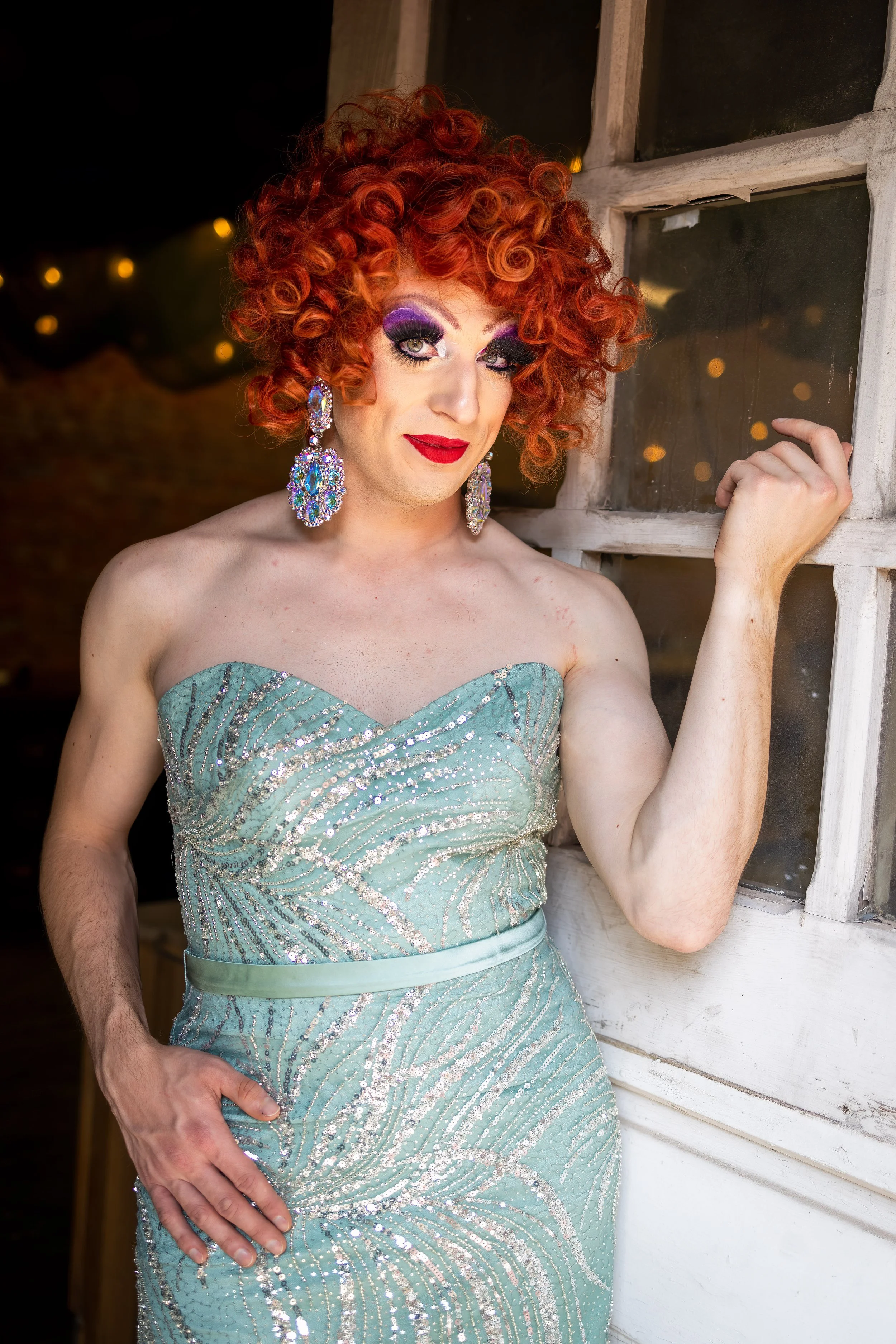 drag queen in sparkly blue dress poses by old white door