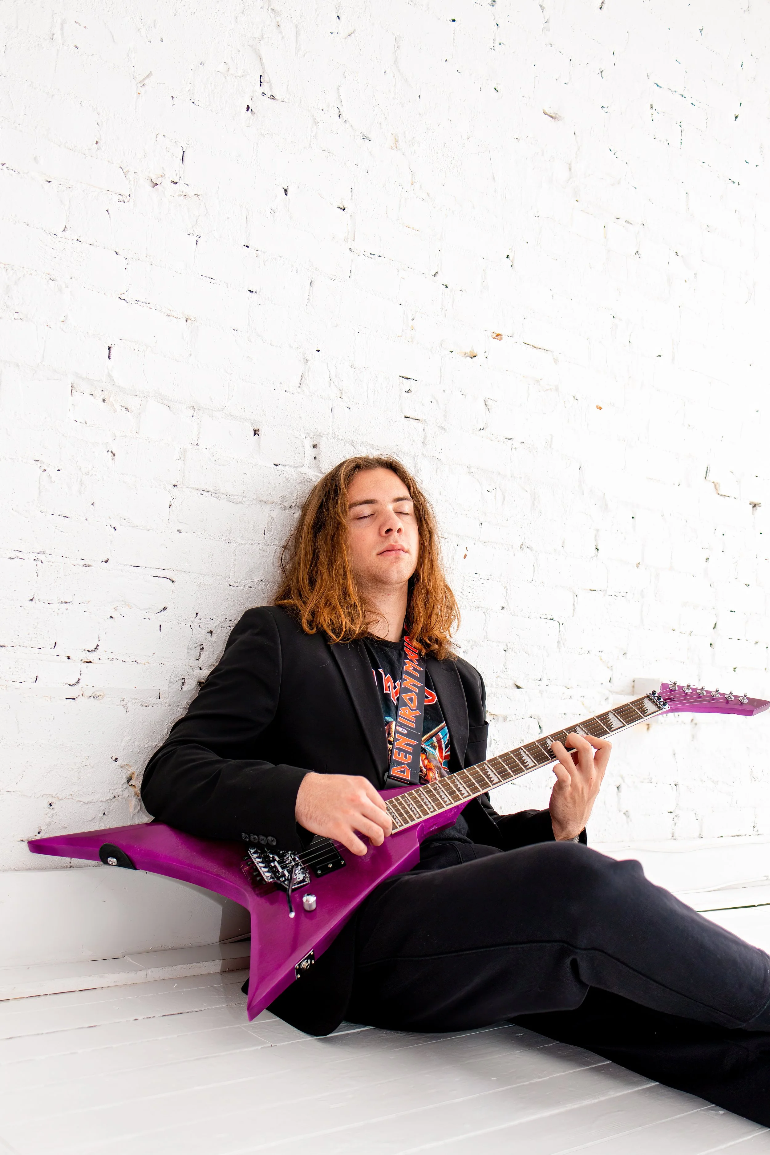 teenage boy closes eyes against wall while playing guitar