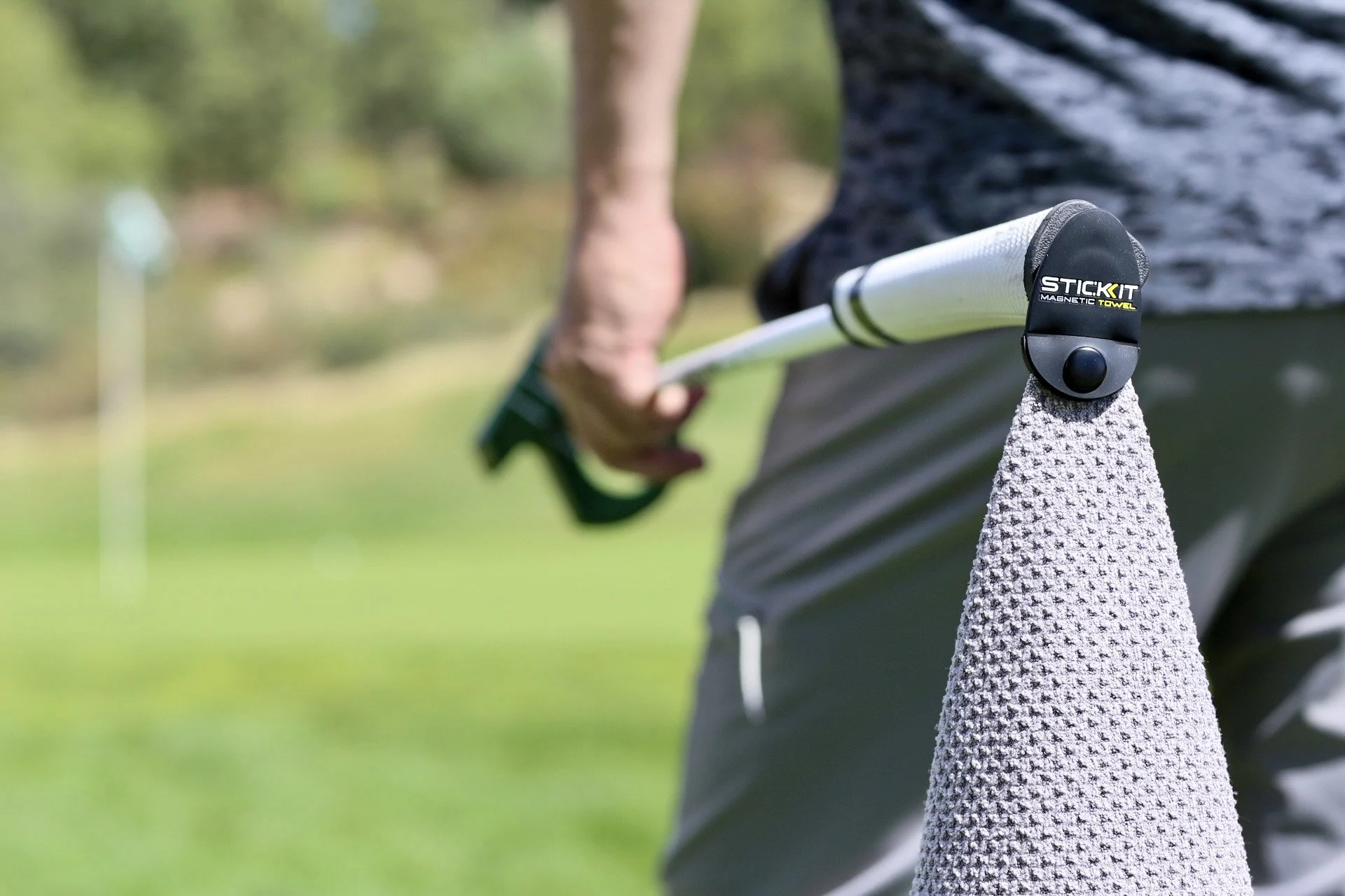 A golfer using a stickKIT magnetic towel on an golf club during a game outdoors.