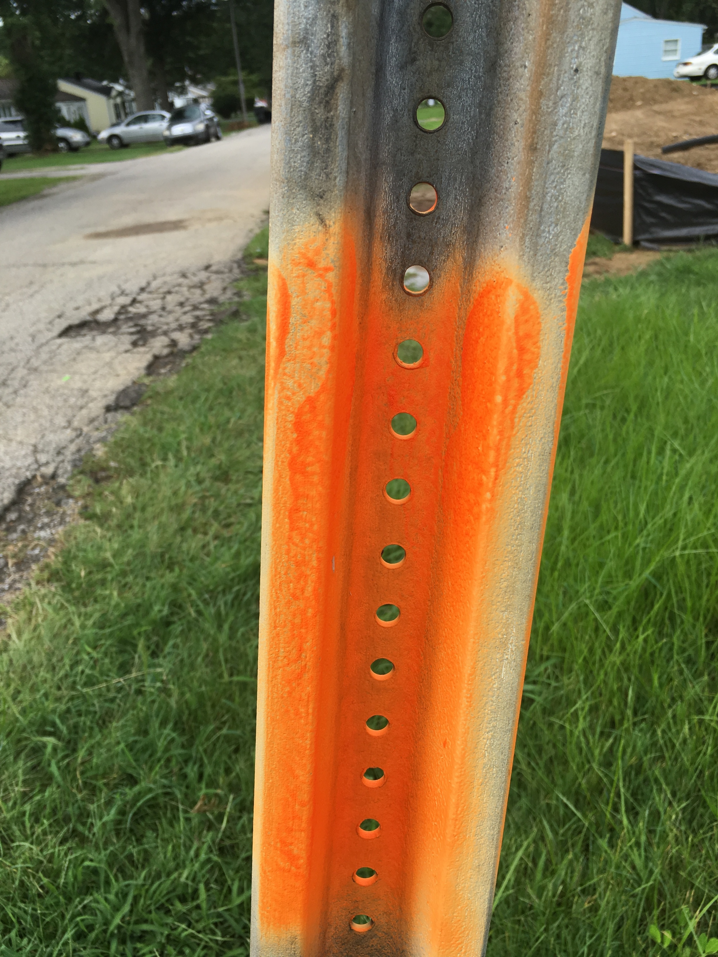 An old and fading sign and street post is marked for replacement.