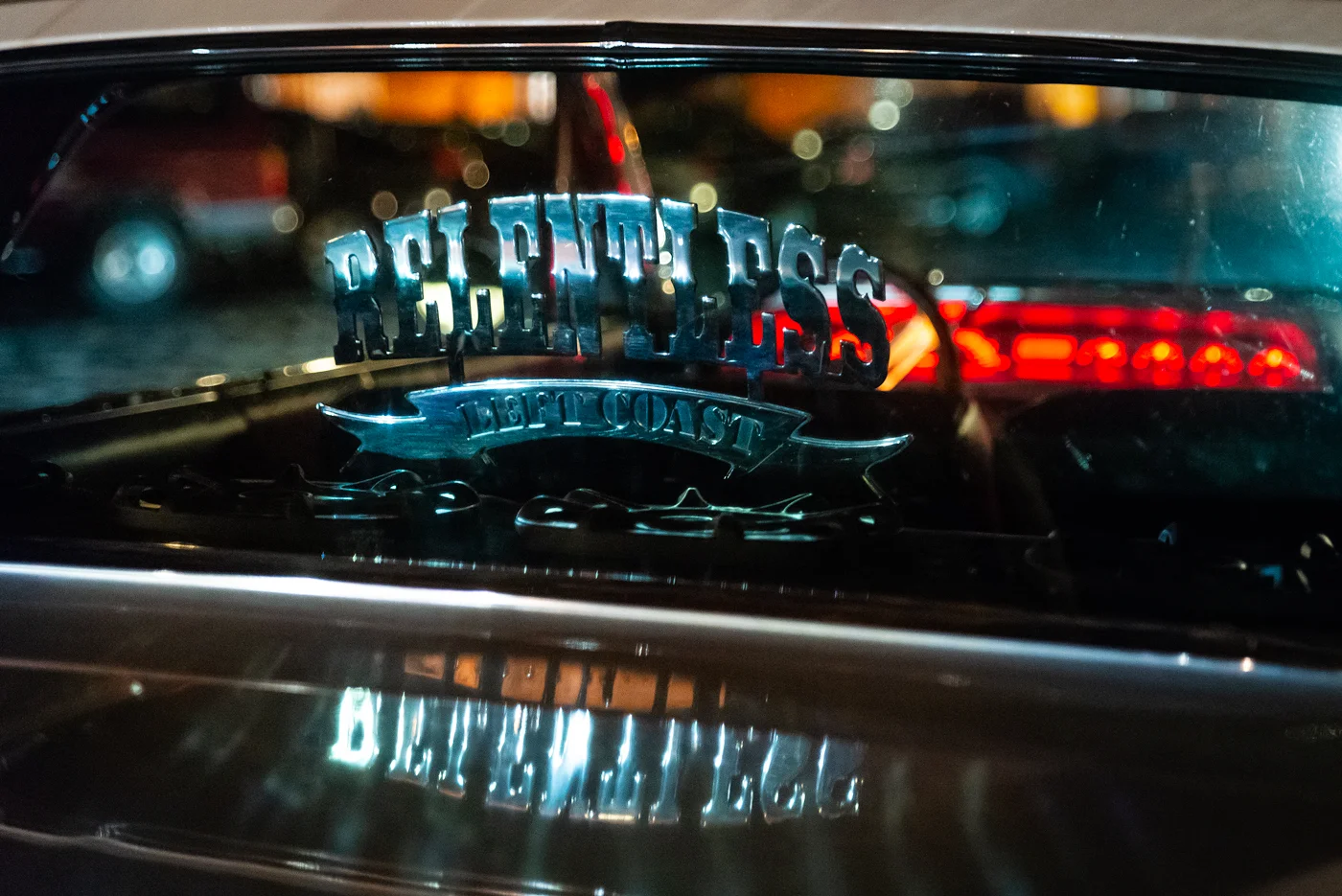 A Relentless Car Club plaque is illuminated by a passing car's headlights as the lowriders in Old Sacramento talk with each other before their final cruise home.