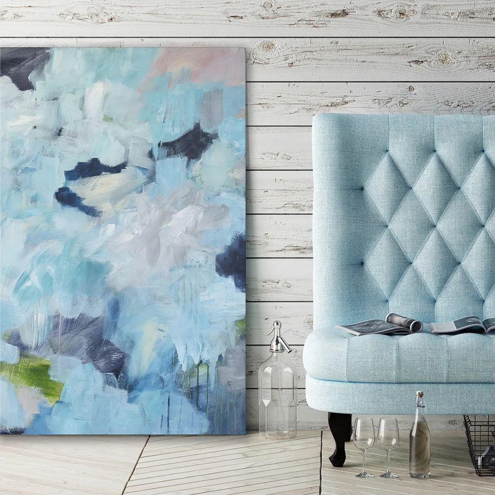 Large blue abstract artwork leaning beside a tufted powder-blue chair in a relaxed coastal-inspired interior.