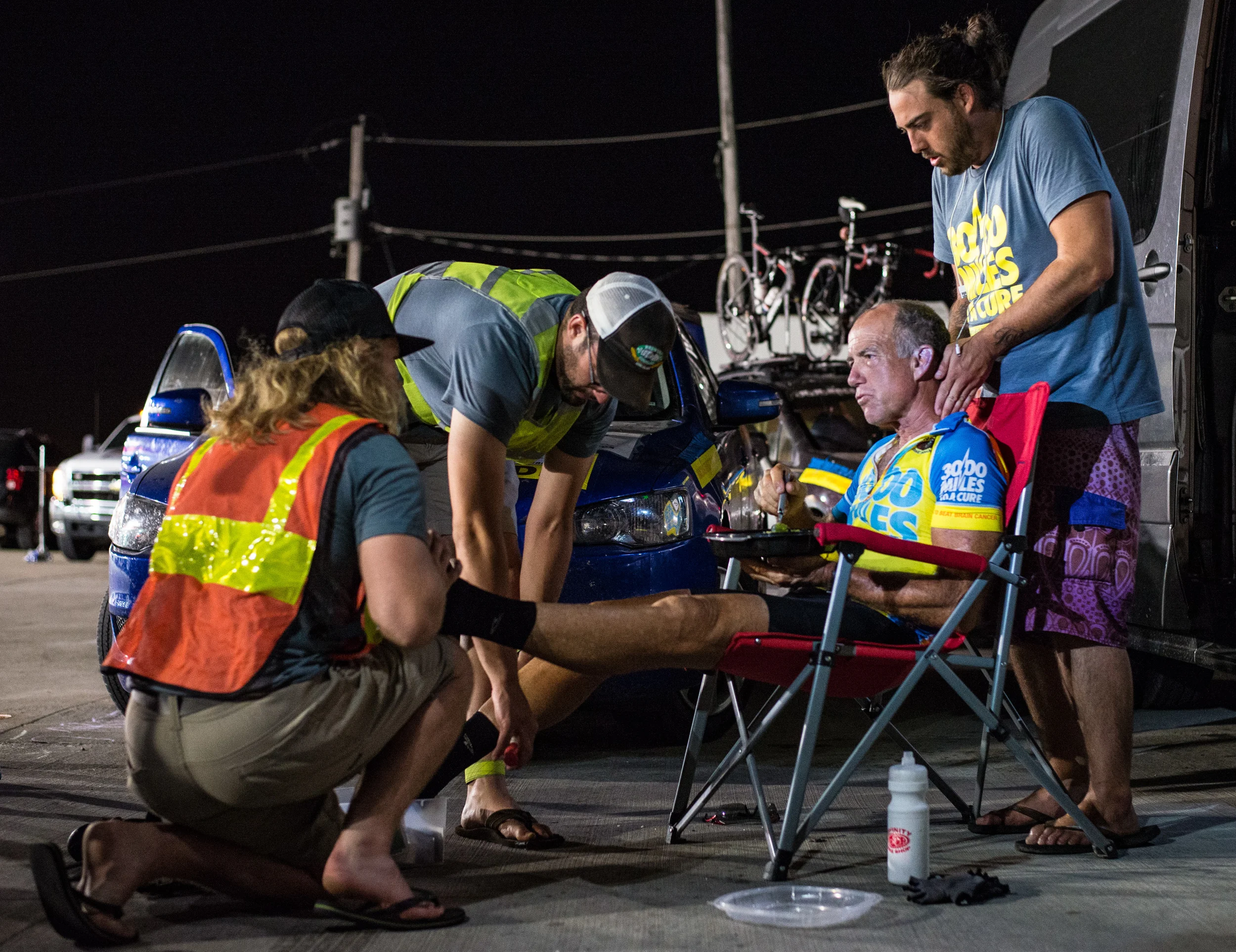 From left to right, crew members Ryan Jean, Tyler Jandreau, and Jesse Reeves massage Marshall as he eats to get him ready for a full night of riding. Marshall had little time to stop as he was trying to make it to the Mississippi River time cutoff. Photo taken on June 22nd, 2016.