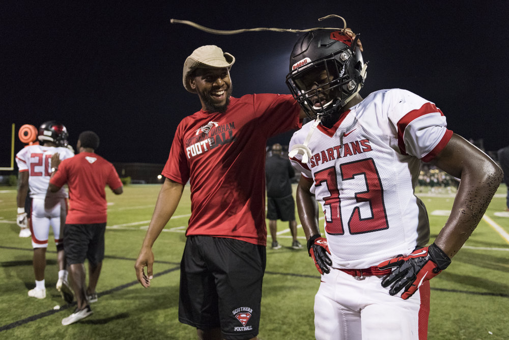  Southern Durham assistant coach Chris Smith celebrates with linebacker Jakhari Dowd (33) after a big play against Cardinal Gibbons High School. The Spartans had 18 coaches on staff this year, mostly comprised of past players that want to give back t