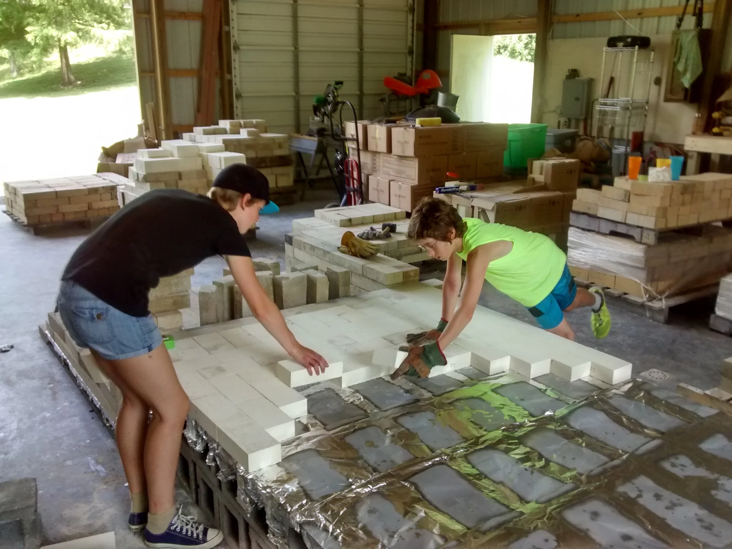 Greta and Michael get put to work laying the insulating brick for the first layer of the floor. Below that are foil to stop moisture and air penetration, and concrete block to further shield the barn floor from the heat of the kiln.