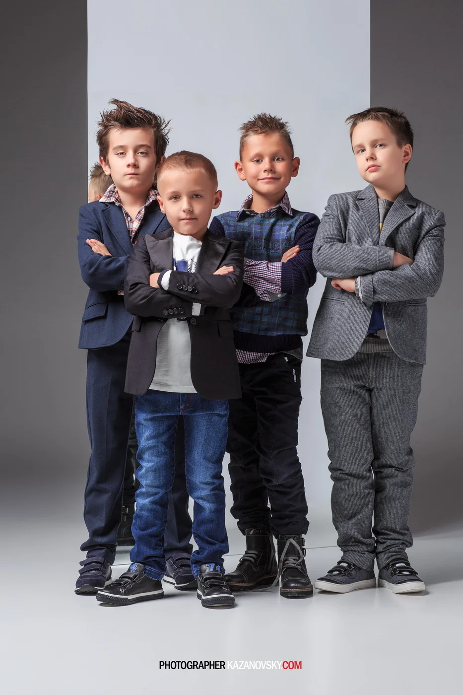 Five young boys standing together with arms crossed, dressed in stylish casual and semi-formal clothing, in a studio setting with a gray background.
