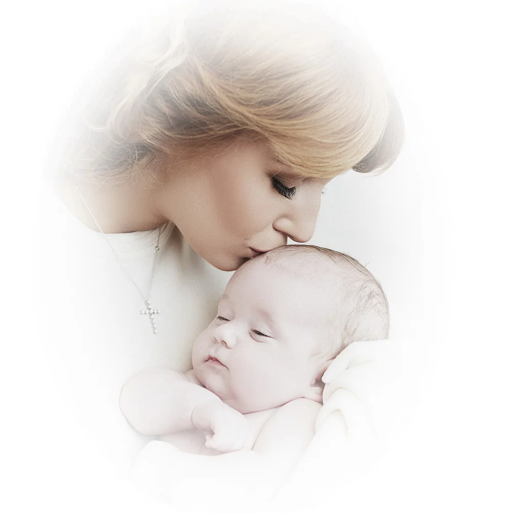 A woman gently kisses a sleeping infant on the forehead.