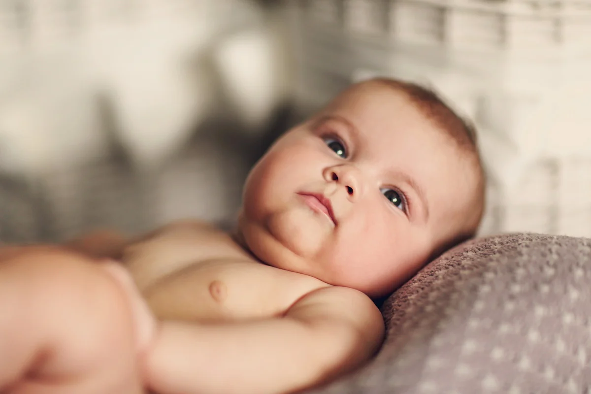 Close-up of a baby lying on a soft surface, gazing up with wide eyes and relaxed expression.