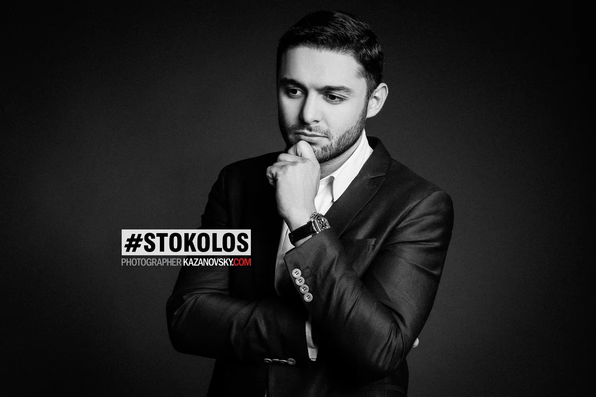 Black and white portrait of a man in a suit with a thoughtful expression, holding his chin with one hand, against a dark background.