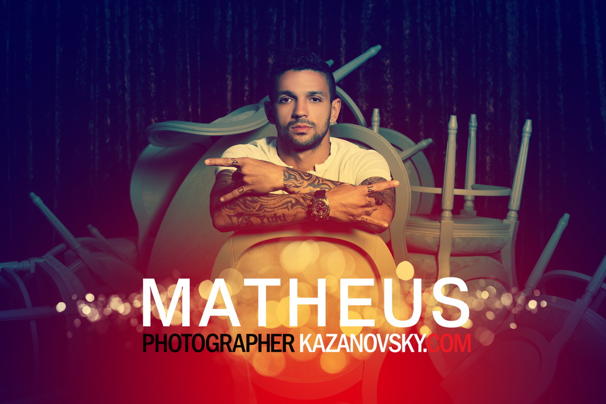 A man with tattoos and a watch making a hand gesture in front of a backdrop of chairs and a dark curtain, with text overlay reading 'MATHEUS PHOTOGRAPHER KAZANOVSKY.COM'.