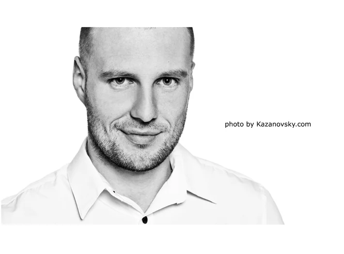 Black-and-white portrait of a man with short hair and beard, wearing a collared shirt, looking at the camera with a slight smile.