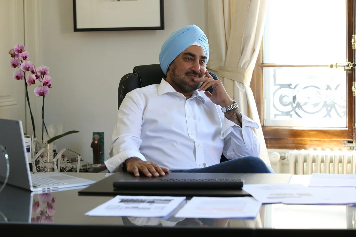 A man wearing a blue turban and white shirt sitting at an office desk, looking thoughtful.