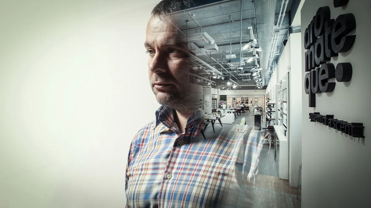 Man looking through a glass wall into a modern, open-plan office or showroom with furniture and displays