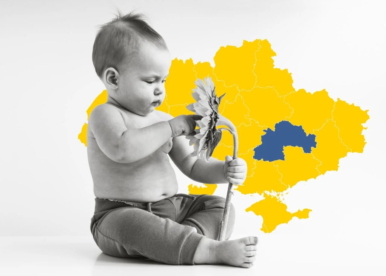 A black and white photo of a young child sitting barefoot, holding a sunflower and a stick. Behind the child is a colorful map of Ukraine with the country outlined and filled with yellow, and a region highlighted in blue.