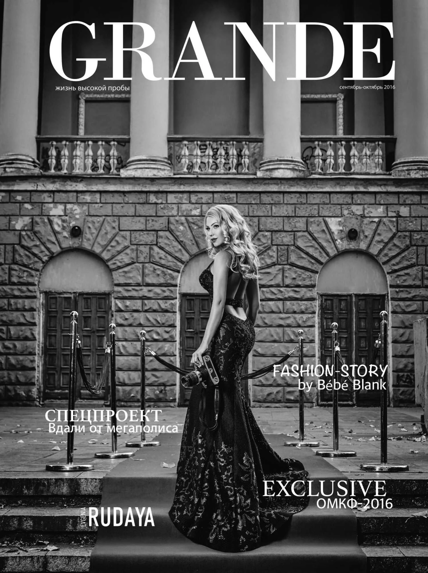 Magazine cover featuring a woman in a black lace gown holding a camera, standing on steps outside a historic building with brick and stone architecture, promoting fashion and special projects.