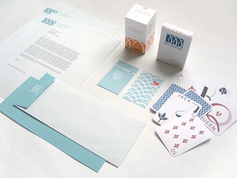  Mock up of potential Millennium brand collateral—business letterhead, matching stationery envelopes, business cards with logo turned into a protective ribcage design, package design, and waiting room promo deck of cards. 
