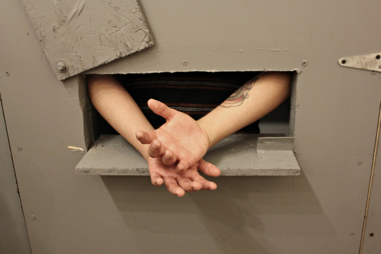 A young organizer poses with his hands extended through the model cell door’s opening, as a prisoner would have to in order to be handcuffed before exiting the cell. (Photo: Kelly Hayes)