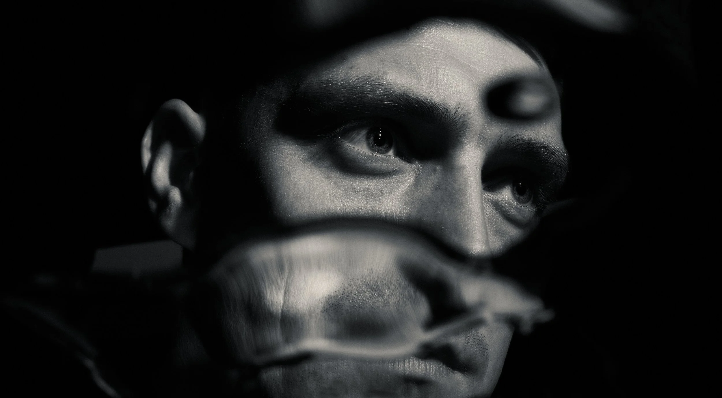 Close-up of a person's face reflected in a mirror, with dramatic lighting emphasizing facial features, black and white photo.