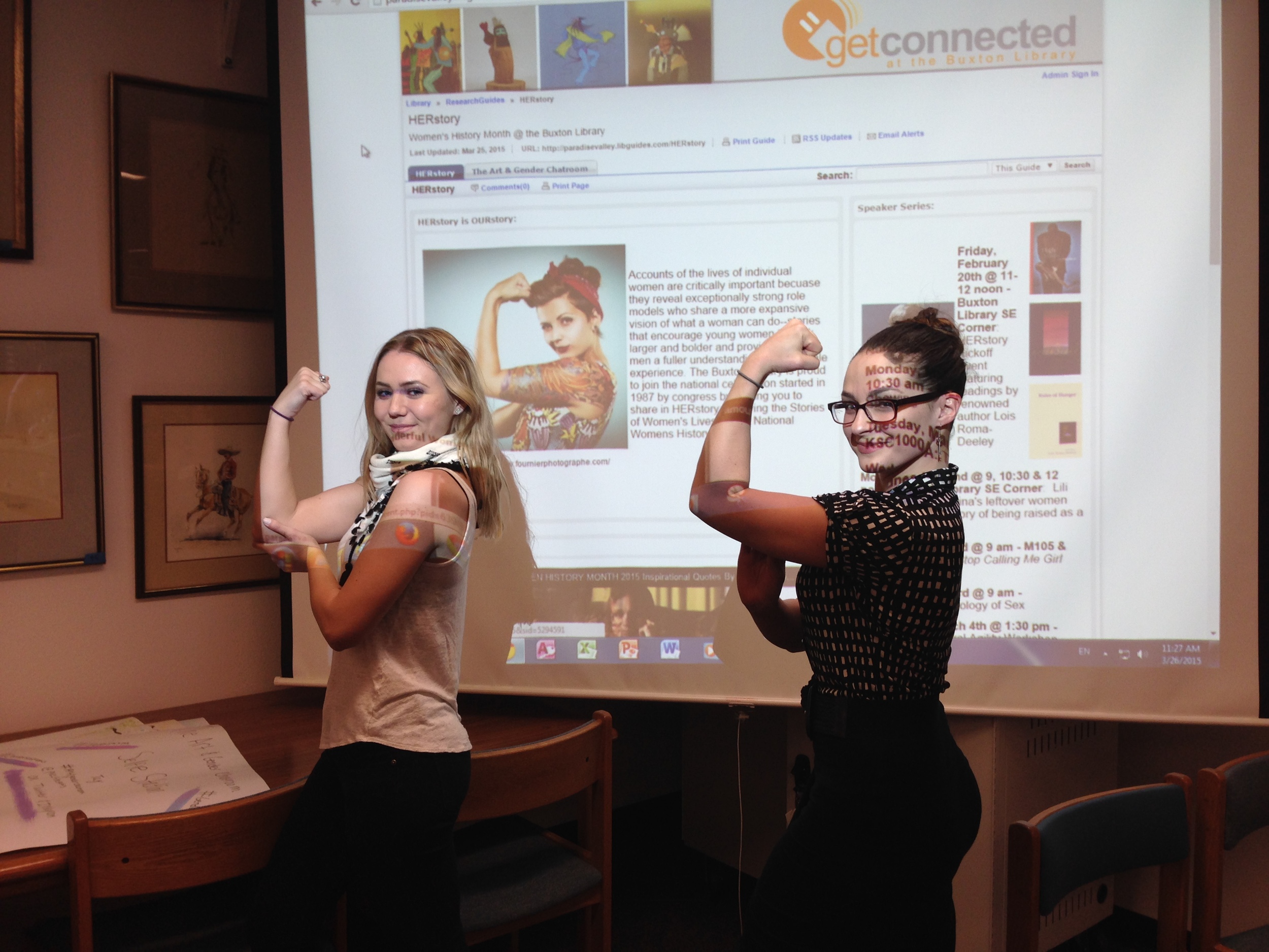 PVCC students Katlynn McNab and Heidi Klotz pose in front of Kande Mickelsen's HERstory blog.