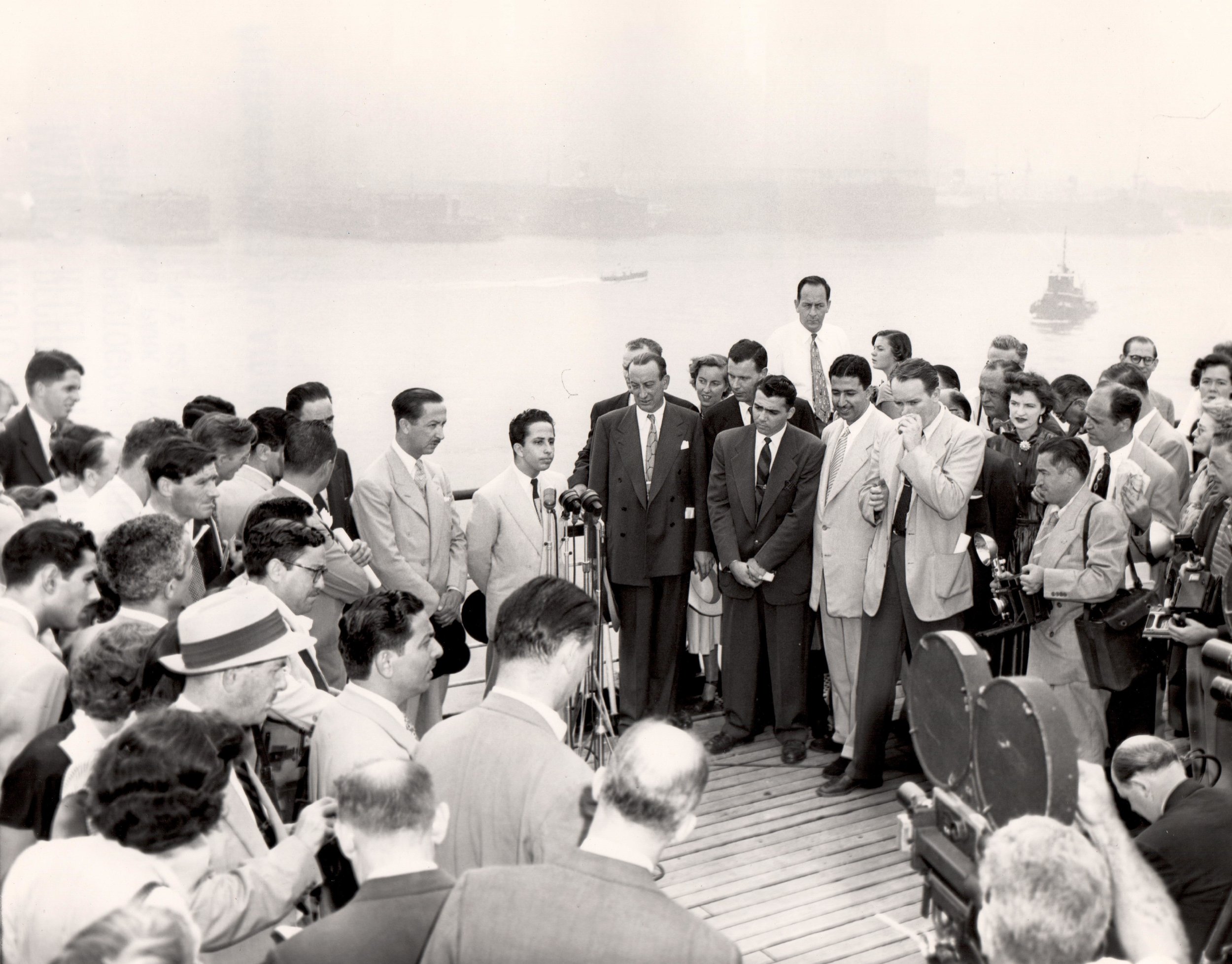 Aboard the RMS Queen Mary King Faisal II of Iraq addressing the press; on the left is his uncle and regent, Abdul Ilah; to the right is John Coleman, Vice Chairman, Mayor’s Reception Committee