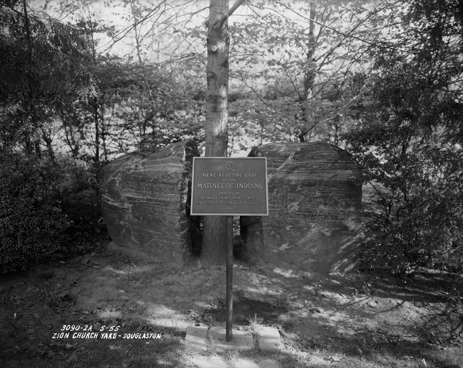 Boulder split in half with carving "Matinecoc" and plaque reading "Here Rest the Last of the Matinecoc Indians Erected by the Major Thomas Wickes Chapter Daughters of the American Revolution-1948." Photo taken at Zion Church Yard, Douglaston, Queens, 1955. Borough President Queens collection, NYC Municipal Archives.