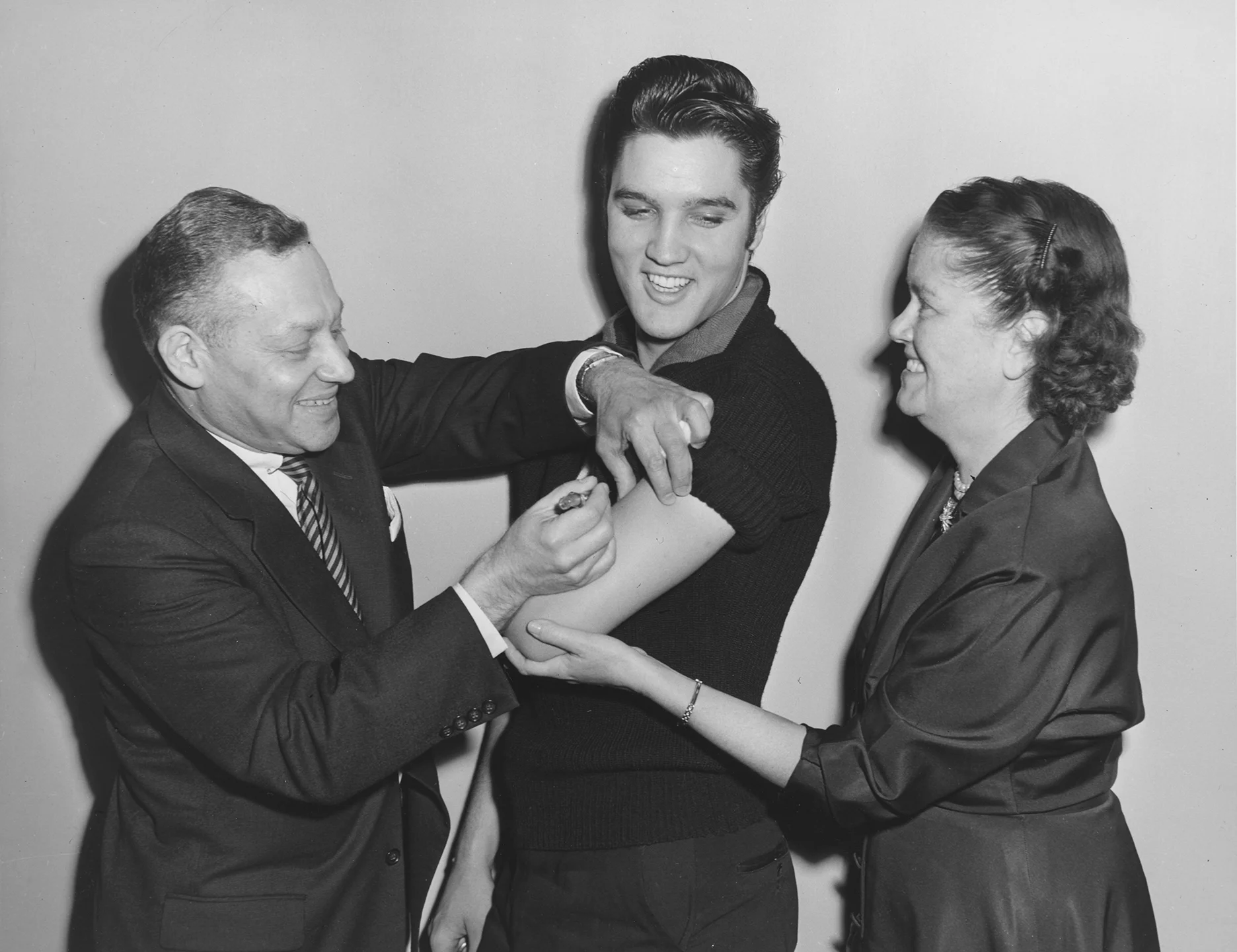 Elvis Presley receiving a polio shot in October 1956 from Assistant Commissioner Dr. Harold Fuerst. Commissioner Baumgartner holds Presley’s arm while Fuerst administers the vaccine. Department of Health Collection, NYC Municipal Archives.