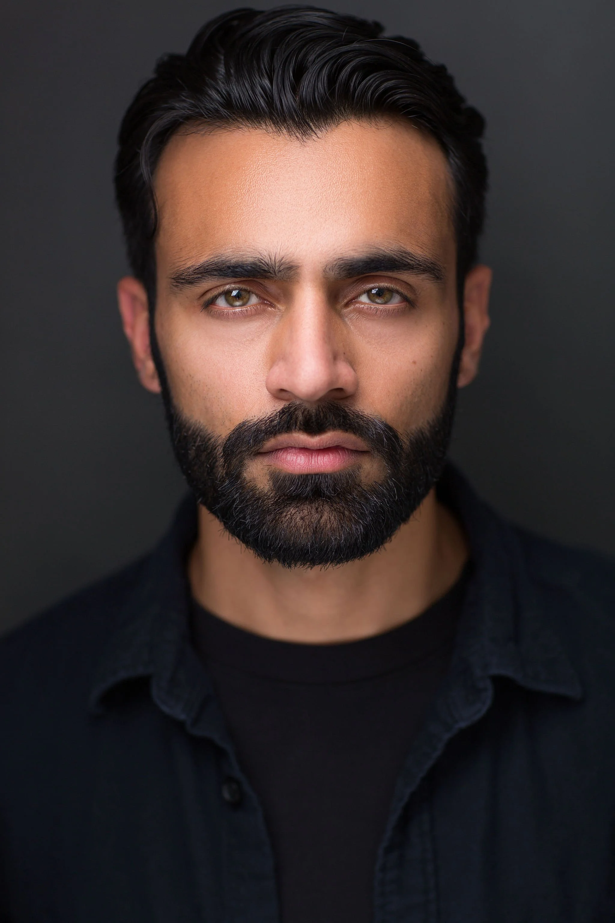 Actor headshot of a bearded man wearing a black jacket against a dark studio background.