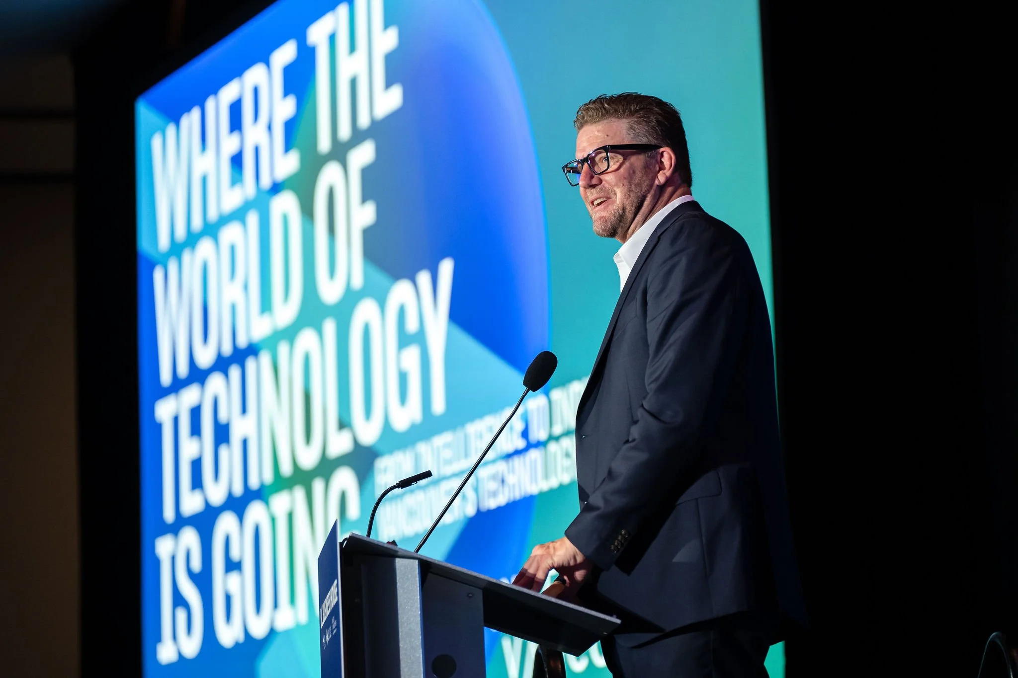 Technology keynote speaker presenting beside a large conference screen