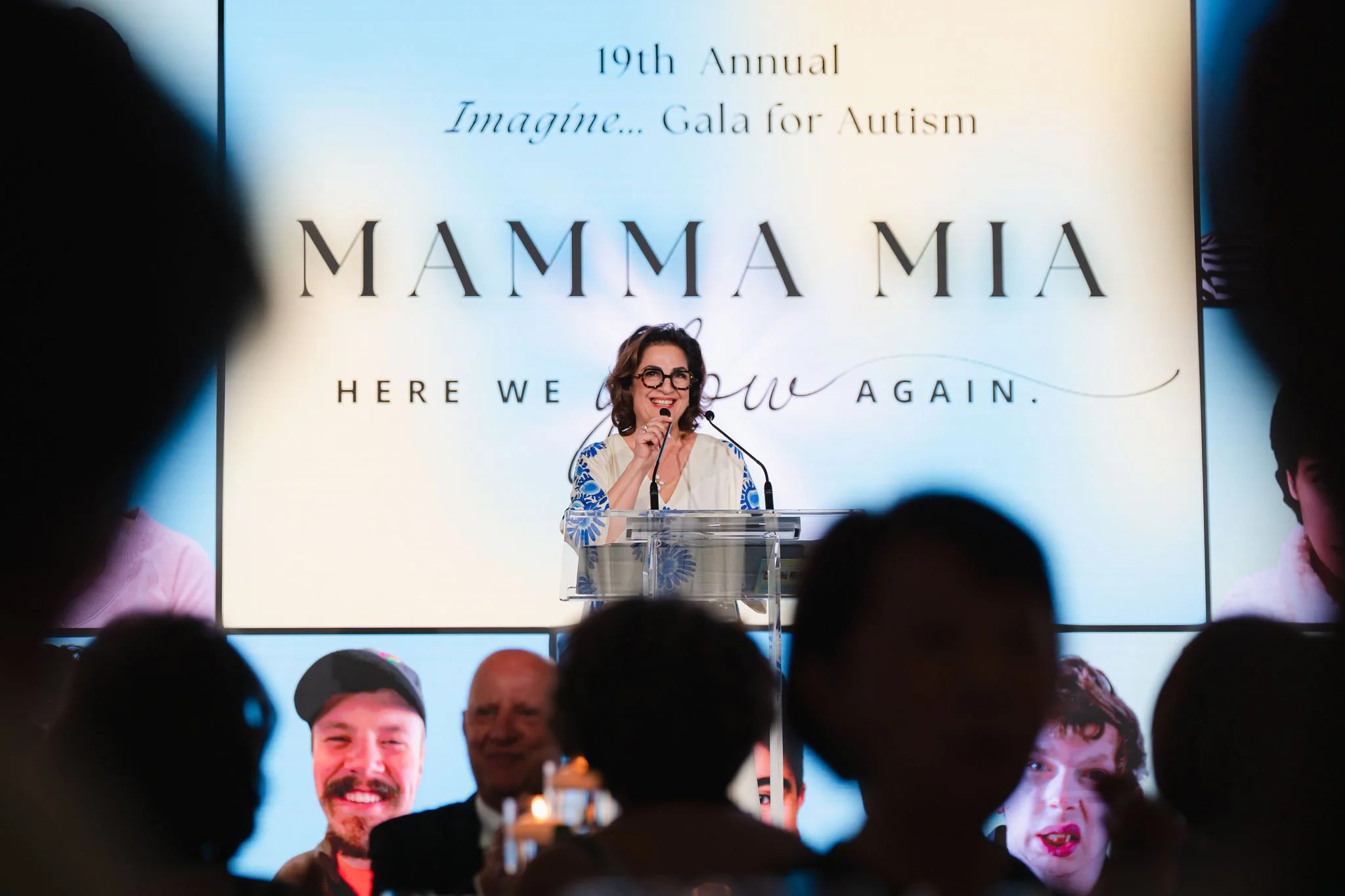 Gala speaker addressing guests beneath the Mamma Mia event screen