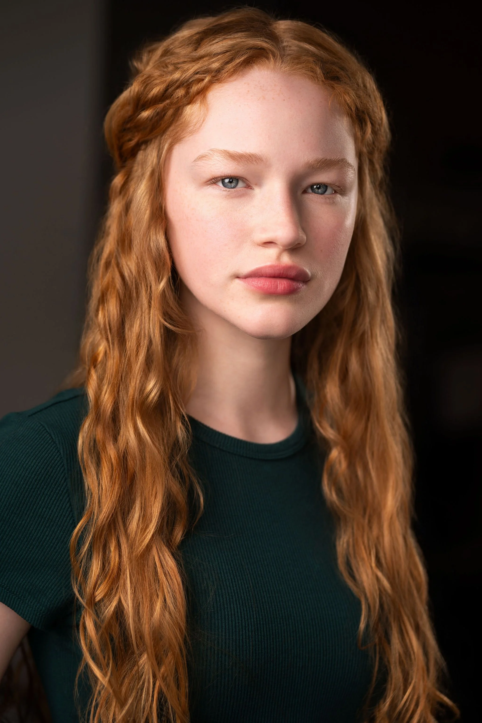 Actor headshot of a red-haired young woman wearing a green top against a dark background.