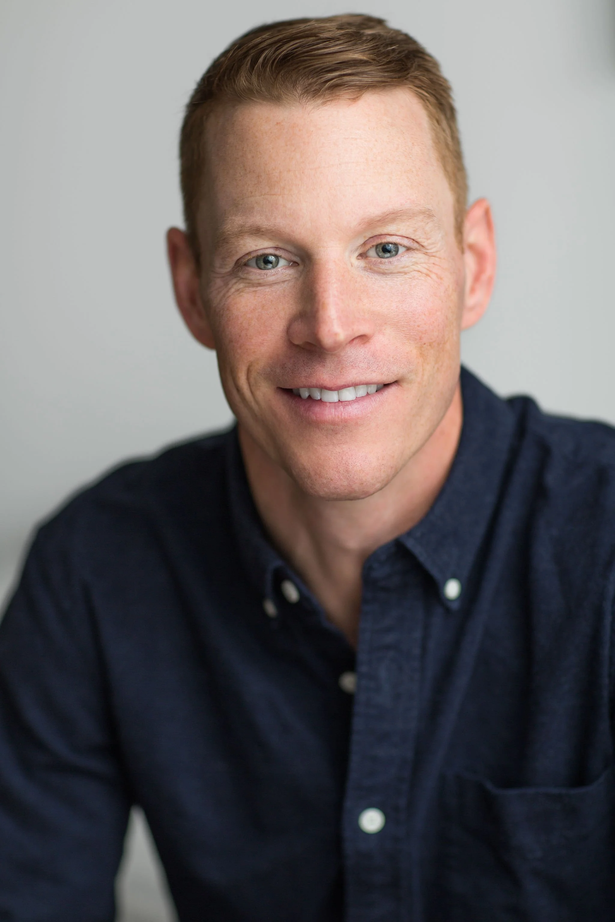 Professional headshot of a smiling man in a navy button-up shirt against a light grey background.