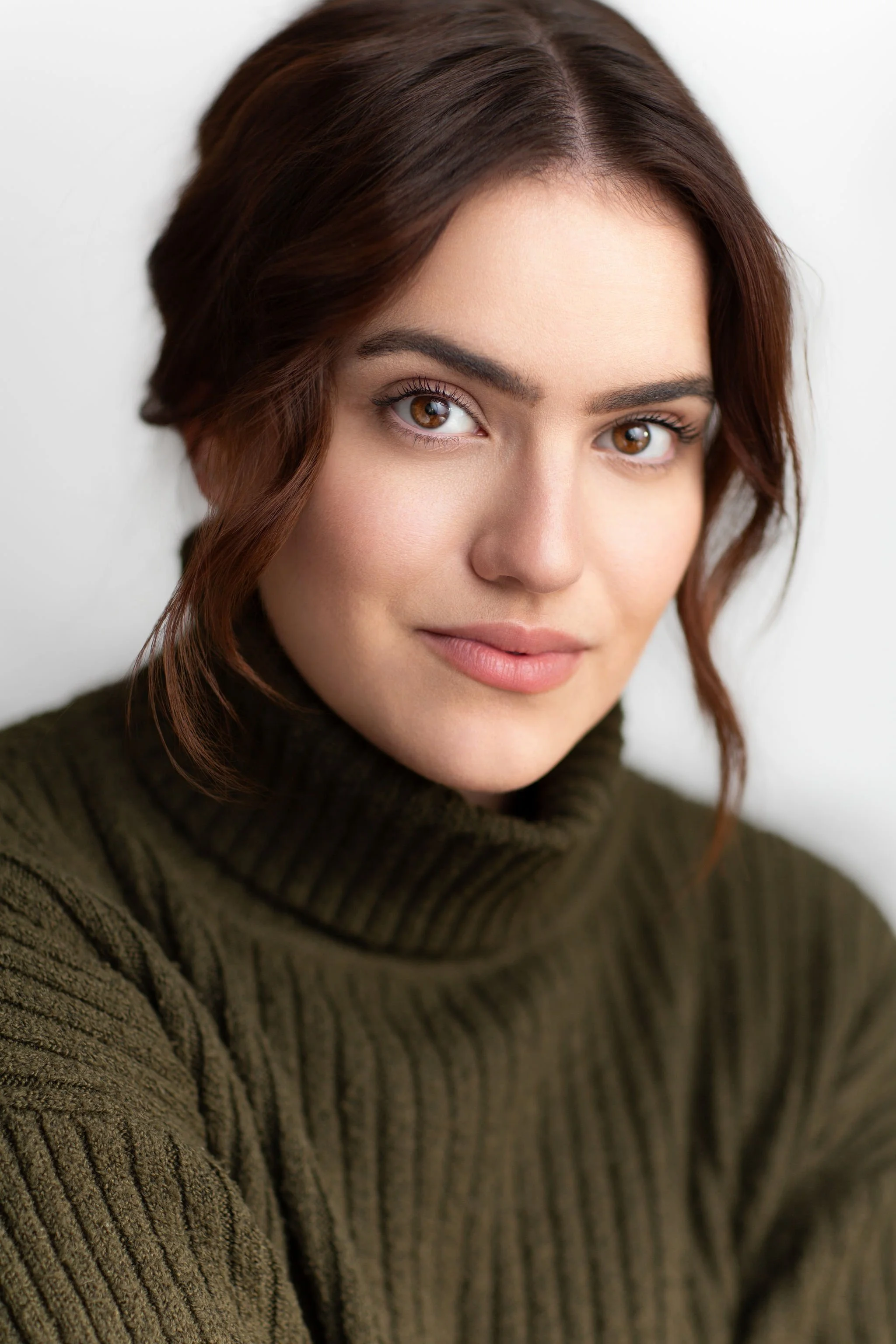 Actor headshot of a young woman wearing a dark green turtleneck against a pale background.