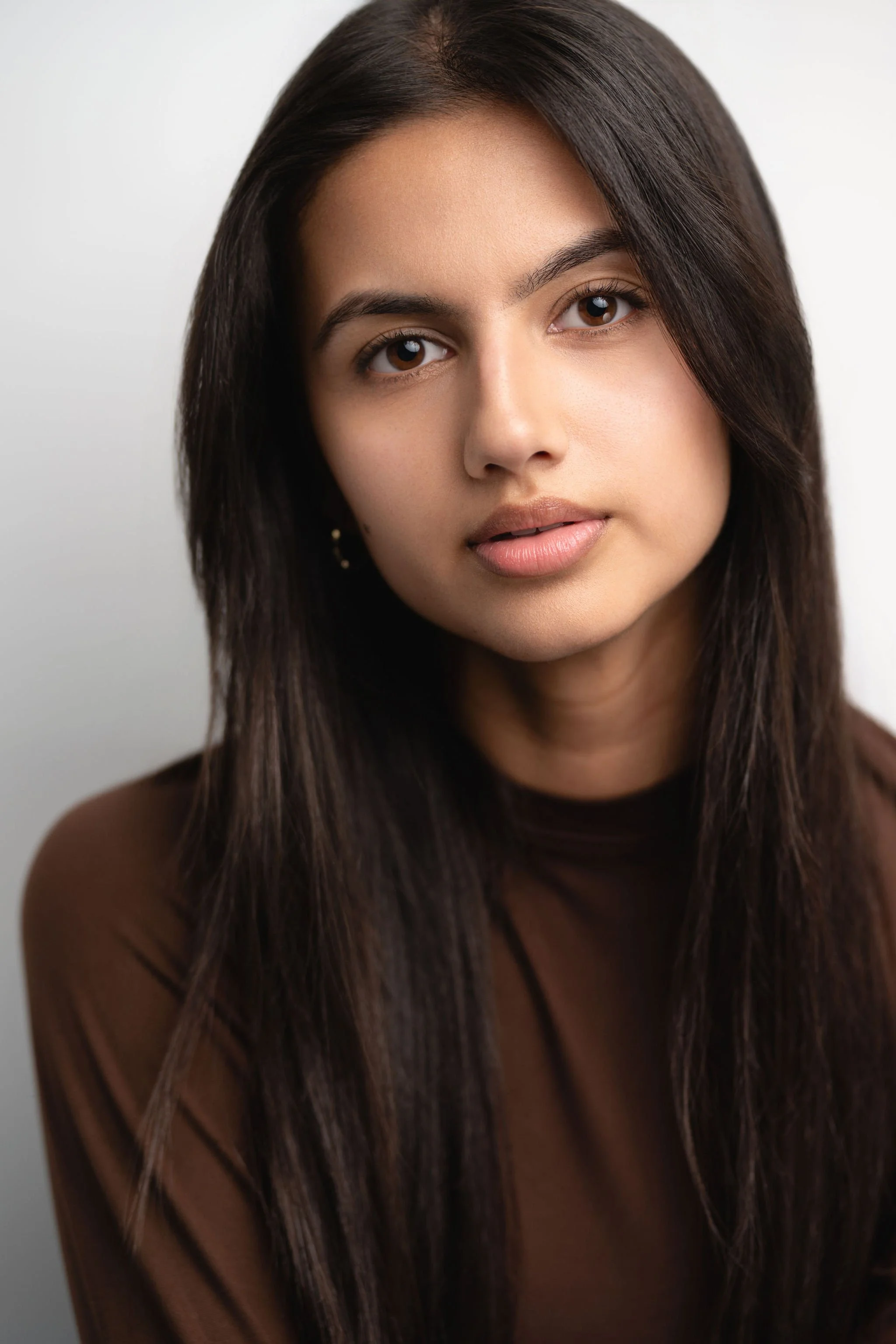 Actor headshot of Justine Sanker wearing a brown top against a pale studio background.