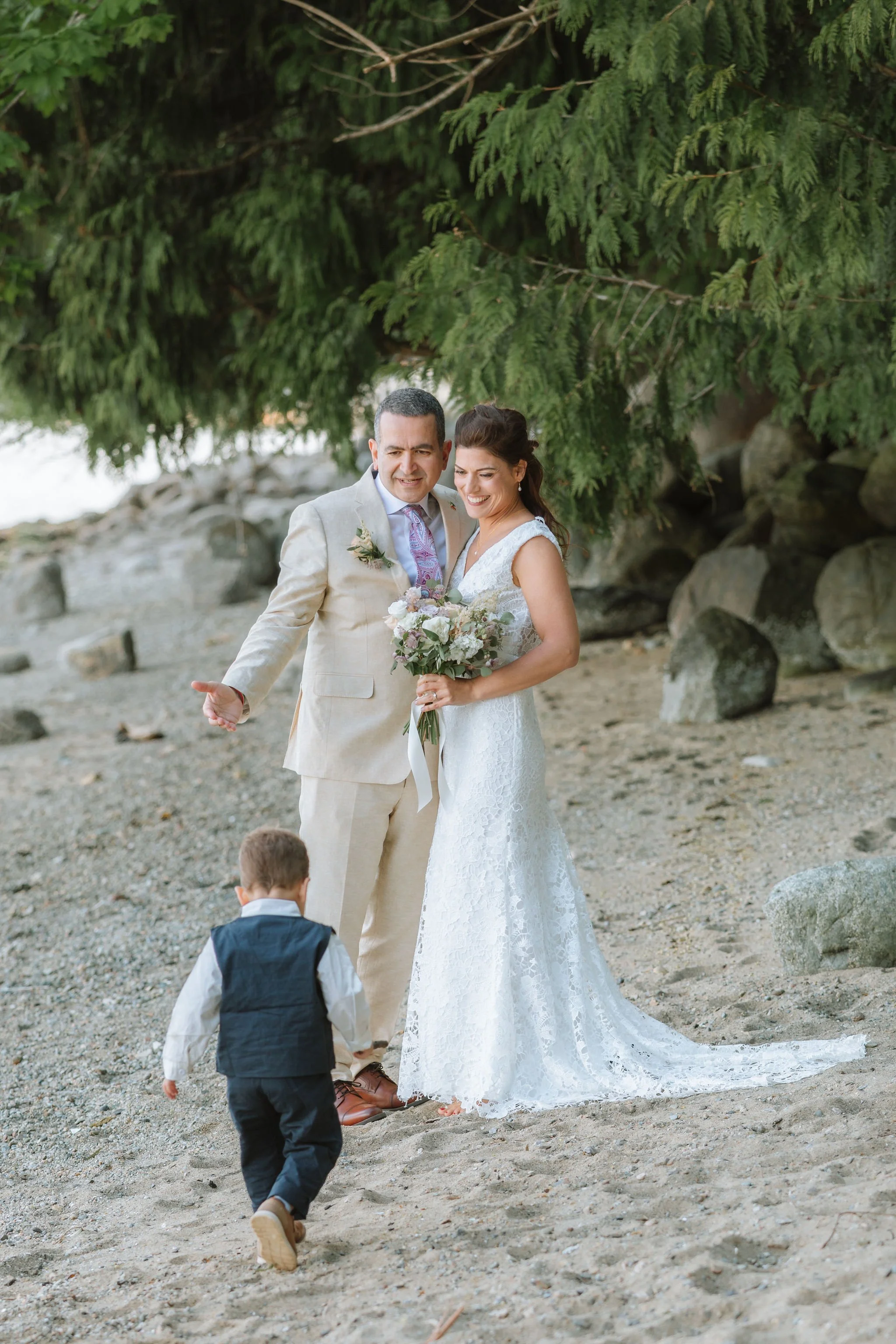 Newlyweds smiling as a young ring bearer walks toward them during a beach portrait.
