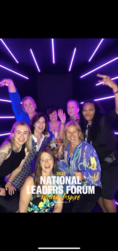 Group of women posing and smiling at the 2024 National Leaders Forum, with purple neon lights overhead.