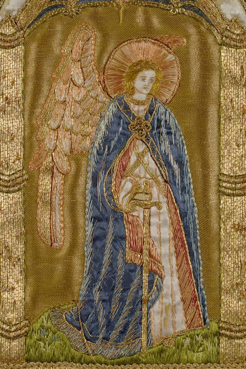 Detail - an angel on the stole, gripping a sword and stood on grass with minute flowers.
