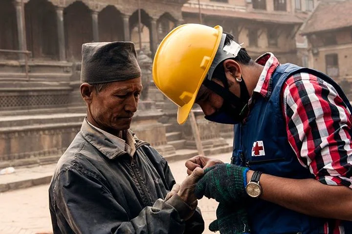 An aid worker from the Red Cross tends to an injured Nepalese man