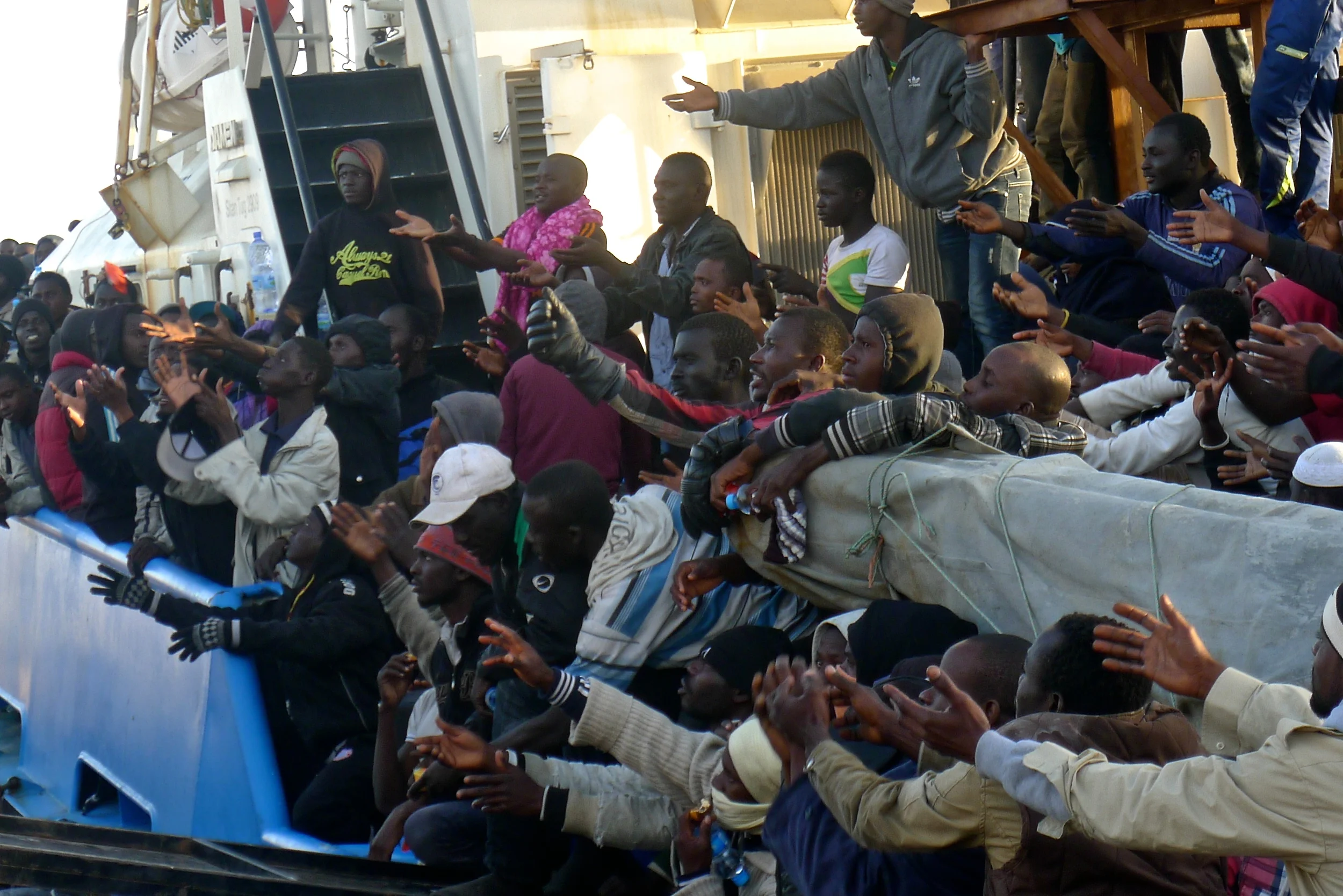 Plus de 400 migrants interceptés par les gardes-côte de Misrata alors qu’ils voyageaient dans quatre bateaux pneumatiques tendent les bras pour attraper des bouteilles d’eau qui leur sont jetées depuis la rive. Nombre d’entre eux ont ensuite été transférés au centre de rétention de Krareem.
